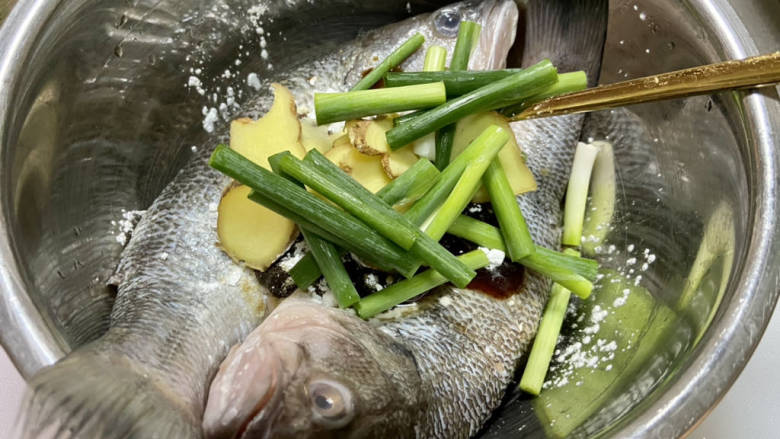 黄豆酱蒸鲈鱼,鲈鱼放入盆中,加入葱白姜片,一汤匙半黄豆酱,一汤匙料酒,一茶匙蚝油,半茶匙白糖,少许白胡椒粉,一茶匙生粉