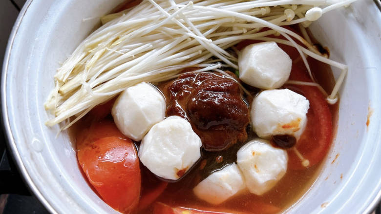 金针菇番茄汤,铺上金针菇和丸子,转大火煮至沸腾。