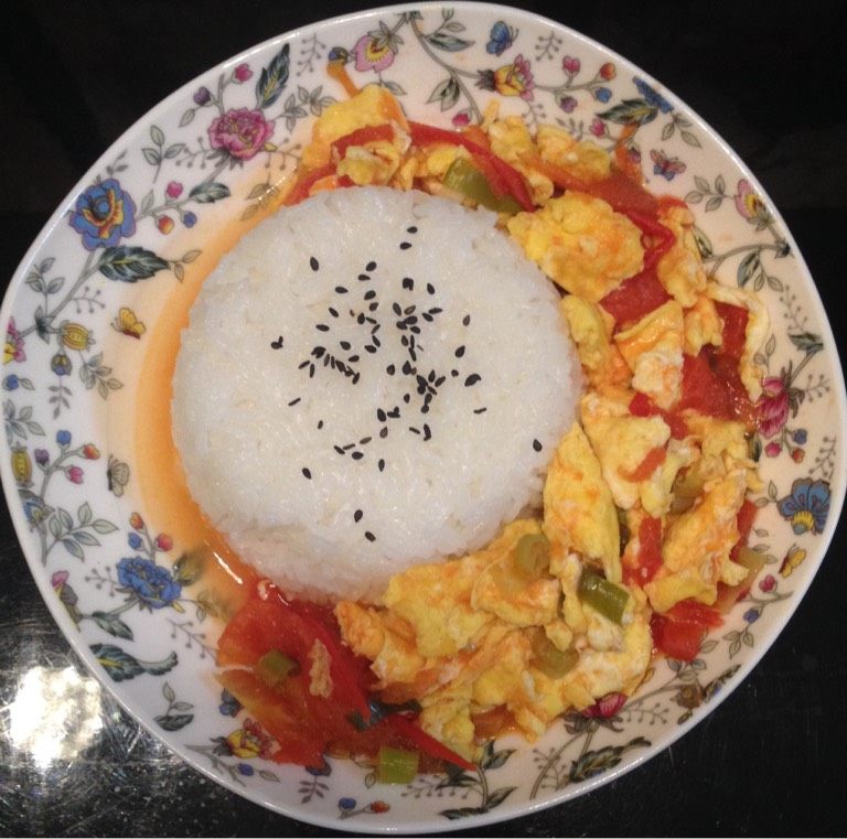 番茄鸡蛋盖饭,盛一碗米饭,压平,倒扣在盘中,上面撒上芝麻,将番茄鸡蛋盛入即可