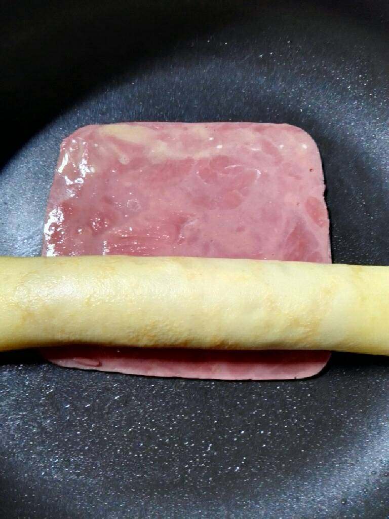 火腿片鸡蛋卷,锅再放一片火腿片,放入刚卷好的鸡蛋卷,(在火腿片前端摸一点鸡蛋液起到粘合作用)再次卷起煎至表面微黄即可。