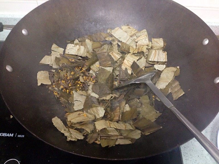 荷熏桂花鸡,取一口无油大锅,倒入荷叶、茶叶和桂花,烘炒至冒烟。