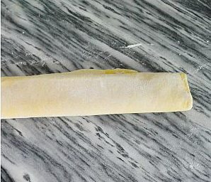 沙琪玛,台面撒上一些干面粉,把面团擀成大片稍薄的面皮。