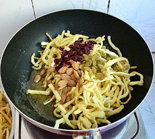 沙琪玛,把炸好的面条倒一半进锅内,再将蔓越莓干、葡萄干、大杏仁也加入,然后再倒入剩下的面条。