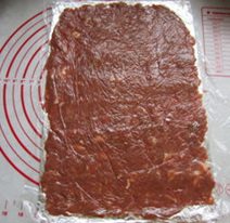 自制猪肉脯,拿出锡纸,放上的肉糜,盖上保鲜膜,用擀面棍擀平。