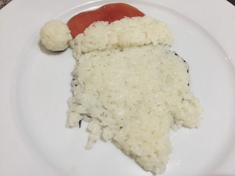 圣诞老人餐盘画,如图帽子和脸之间的帽檐用米饭填满,注意要做出层次感高于脸部,用保鲜膜包裹米饭做成圆球,做成圣诞老人的帽子圆球装饰