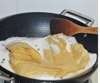 盐焗鸡翅,腌制好的鸡翅用两层油纸包起来,埋入炒锅中炒热的盐中。