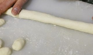 泡菜意大利面疙瘩,把处理好的土豆泥放到木板上,在木板上撒上一些面粉;双手搓揉直至面团光滑;将大面团分成拳头大小的面团,将其擀成约3厘米厚的长条。