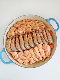 三汁焖锅,腌渍鸡翅、鱿鱼和大虾时放入的葱姜拣去不用,然后将鸡翅、鱿鱼和大虾铺在蔬菜丁上面,然后将味淋均匀的倒在食材上。
