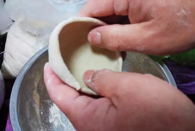 莜面大蒸饺,取乒乓球大小的一块面团,用手捏成圆窝窝状,这样装馅儿方便,收口容易。如果擀成像饺子皮一样平平整整的面片来包大蒸饺,一是包的馅儿不会太多,二是因为面皮没有筋性,收口的时候十分容易“露馅儿”。捏好的圆窝窝不能太薄,否则蒸熟之后会“化”开。因为莜面没有筋性,在蒸时遇水易“化”。