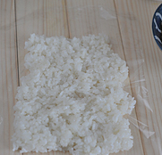 粢饭团,用勺子沾凉开水防粘,舀一团米饭到保鲜膜上,用勺子摊开按压紧