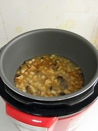 鸡汤菌菇焖饭,将炒好的蘑菇连同汤汁倒入电饭煲,用勺子将蘑菇铺匀。