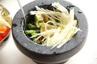 泰式青木瓜沙拉,加入钵中敲打。左手拿个大勺子,右手拿着棒槌,边敲打边用勺子搅拌