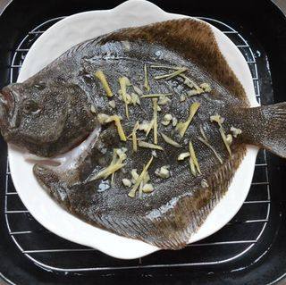 清蒸多宝鱼,锅里烧开适量水,把多宝鱼放进,并在鱼肚和鱼身上放上适量姜丝和蒜粒。盖上锅盖大火蒸13分钟。
