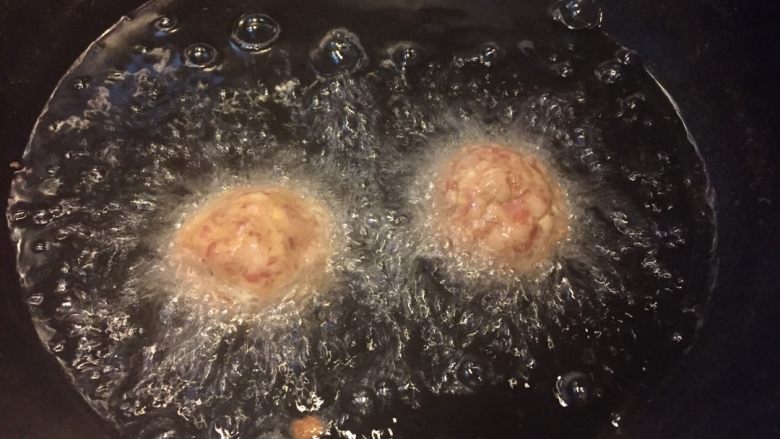 红烧狮子头,如图锅中加入没过丸子的油加热,将鸡蛋和淀粉混合液裹满丸子,入油锅大火炸制