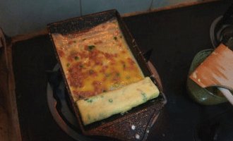 玉子烧,卷到头后将卷子推回,再继续倒蛋液,用相同的方法,连同之前的卷子一起向前推卷,重复这样的动作3-4次即可盛出。整个玉子烧卷好后,翻动整个稍微蛋卷煎一下,使其边缘封紧。