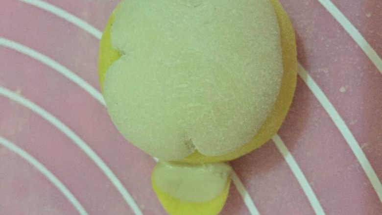 南瓜小猴子馒头,发酵好的面团取一块黄色的面团揉成光滑的圆形,做小猴子的头,取一块略小的白色面团按成饼,用勺子把分别从两边和上边向里推出弧度做猴子的脸,将白色面饼抹点水和黄色的面团按压在一起,注意不要压扁,取两块黄色面团和白色面团做成小猴子的耳朵