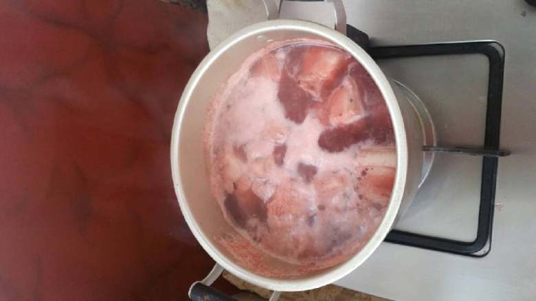 砂锅红烧猪肉芋头,锅中加水,将切块猪肉与适量红曲米冷水下锅,将猪肉焯水去除血沫并初次着色。