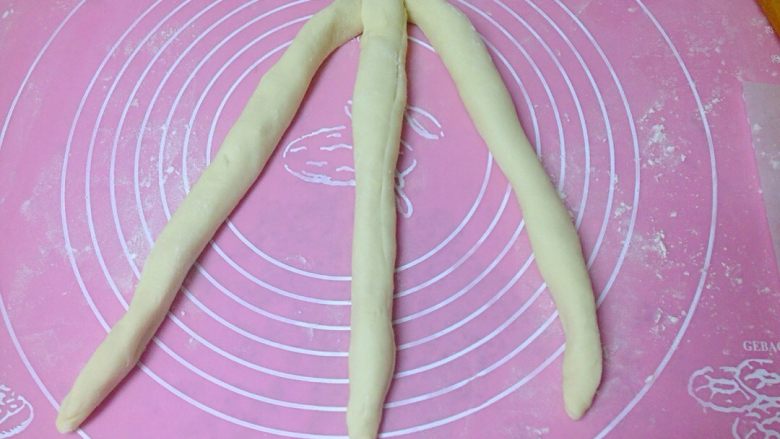 椰香奶酥辫子面包,把面皮纵向卷起成长面卷。每3根长面卷一组,顶端合拢捏紧。