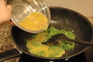 香煎菜脯蛋,用铲子将韭菜花在锅底铺匀,然后缓缓倒入蛋液;