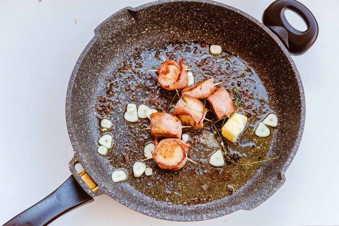 培根扇贝卷,等一面煎至金黄后再翻面煎另一块儿，锅中放入香草