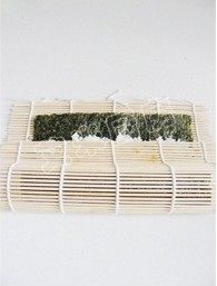 紫菜包饭,将竹帘卷起,先将米饭上的鸡蛋萝卜等卷起,卷起之后用双手均匀的将卷好的部分捏紧