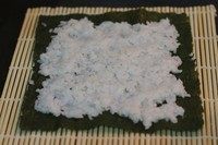 鳗鱼寿司,将一张比海苔稍微大一点的保鲜膜铺在竹帘上,放上一张海苔,铺上薄薄的米饭