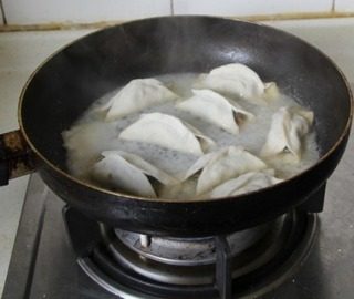 猪肉豆角锅贴,沿锅边淋入冷水,浸没锅贴三分之二左右,盖锅盖焖3分钟左右水干揭盖即可