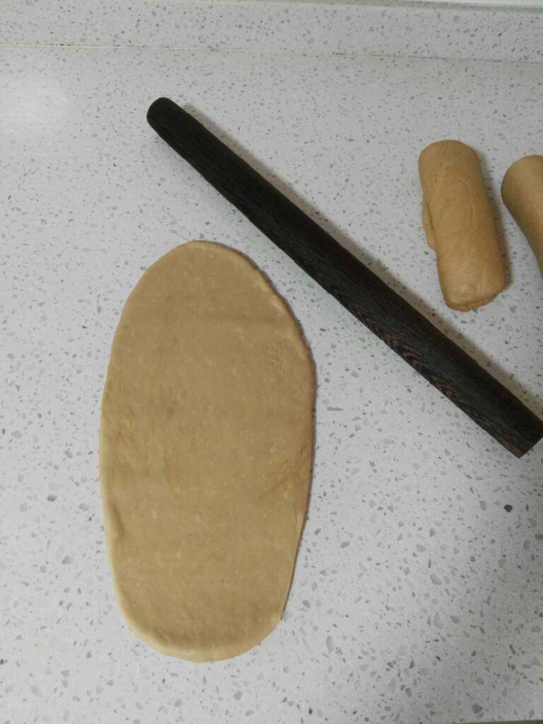 奶咖糯米粉吐司,发酵好的面团,取出挤压排气,均匀分成三等分,滚回不必松弛,直接擀开成椭圆形,卷起2个圈,盖保鲜膜松弛15分钟。