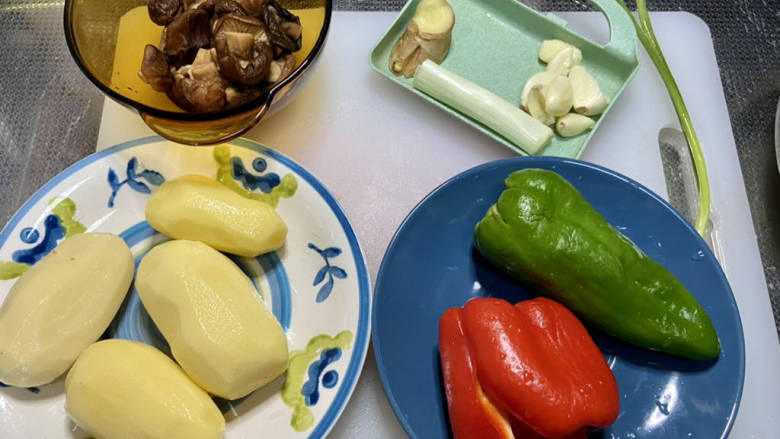 土豆香菇焖鸡,土豆削皮洗净,泡发好的香菇搓洗干净,攥干水分,红椒青椒去蒂去籽洗净,姜搓洗干净,葱白小葱洗净