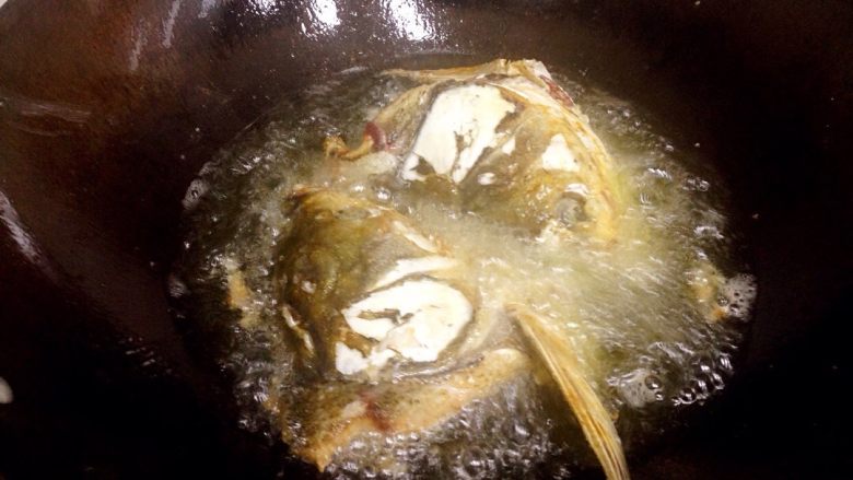 冻豆腐焖鱼头,锅内倒入足量食用油,烧热,放入鱼头大火炸至两面焦黄,捞起备用。