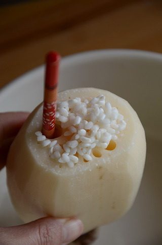蜜汁藕,拿一个大碗接着,将泡好的糯米灌入藕孔,一边灌一边用筷子压实