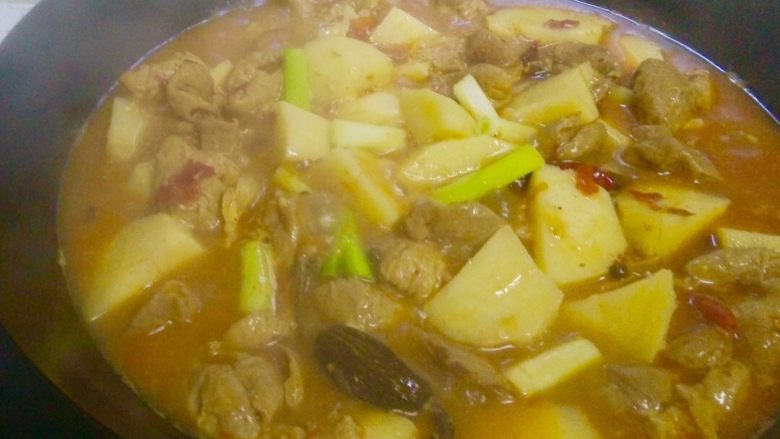 地方菜-土豆烧肥肠,翻匀后盖上锅盖,中小火继续煮约15分钟左右,待土豆熟透变软即可。提前两三分钟放入大葱段,继续煮至汤汁收浓。