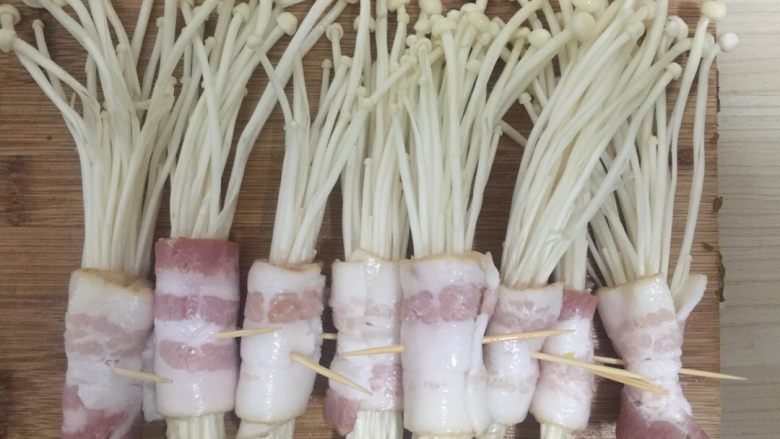 香煎金针菇培根卷,然后把培根放在切板上，金针菇放在培根上面，培根从一端卷到另一端，最后插上牙签即可。