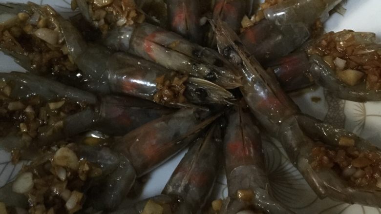 蒜蓉蒸大虾#健康美颜餐#,用勺子把炒好的蒜末放进虾的后背,摆盘,多余的蒜末倒进盘中央。(厨房的灯不给力,有点黑)