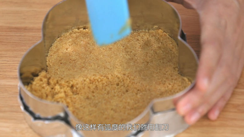 蓝莓益力多慕斯,把混合好的饼干碎倒进去包好底的慕斯圈里面,铺平,然后用刮刀把饼干碎压平压紧压实,饼干底就做好了,然后把饼干底送入冰箱冷藏室凝固一下备用