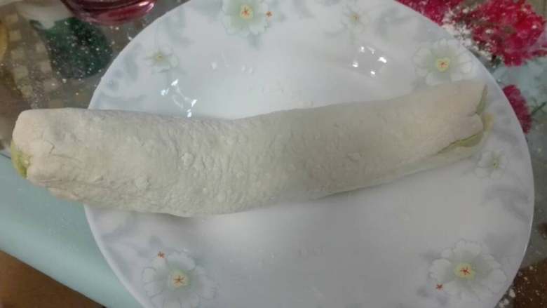 翡翠猪肉水饺,将白色揉好的面团用擀面棍擀平，绿色的面团搭在上边，再用擀面棍擀，后卷起来，如图一样，切成小块，同样用擀面棍把皮擀好就可以了。