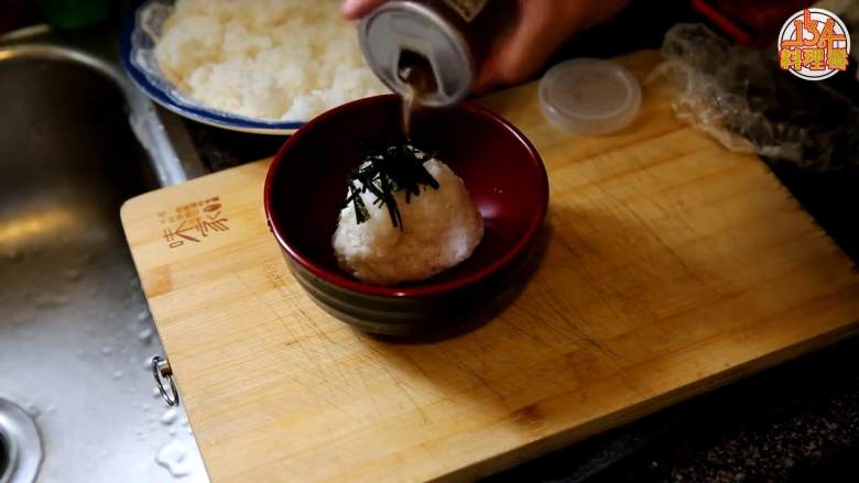 三文鱼饭团茶泡饭,撕下保鲜膜，撒一点盐，把饭团按在碗中，要保持立着的形状，铺上一层<a style='color:red;display:inline-block;' href='/shicai/ 279'>海苔</a>丝，倒入下饭料