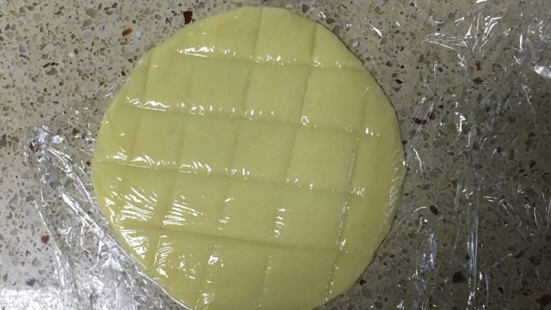 汤种酥皮菠萝包,酥皮造型:把等份的酥皮用保鲜膜上下包住后用擀面杖擀成如图大小。再用刀背在圆形酥皮上留下类似菠萝的印记。注意不要切断。