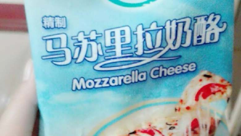 果蔬披萨,奶酪稍微软化，刨子削丝。均匀的撒在布满番茄酱和千岛酱的披萨上，然后加入准备好的材料，在材料上加多一层奶酪丝