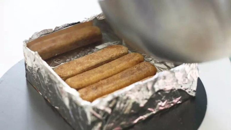 提拉米苏,用锡纸包住慕斯圈,将刷好咖啡密的手指饼干铺在底部。