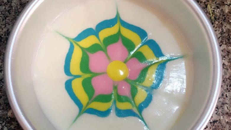 炫彩酸奶慕斯,绿色慕斯糊和粉色慕斯糊轻轻镇动使其扩散,用牙签在慕斯糊中间位置向边缘均匀的画出五条直线,再从两条线的中间从慕斯糊边缘向中间画五条直线,一朵可爱的彩色花朵就形成了,滴入黄色的慕斯糊入冰箱冷藏四小时。