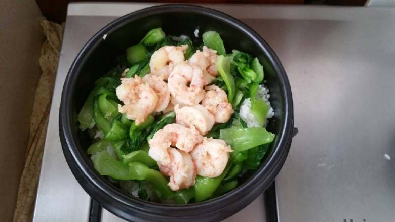 石锅芝士海鲜拌饭,米饭上铺匀小油菜,放入炒好的虾仁。