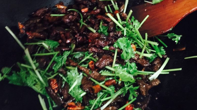 干煸麻辣牛肉丝,将煸干的牛肉放入锅中翻炒,然后加入香菜,盛出