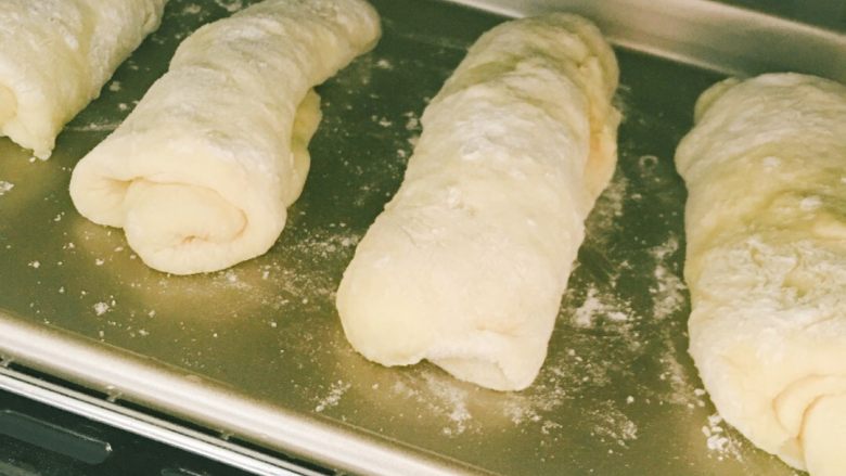 鸡蛋牛奶排包,准备烤排包的烤盘，刷上一层黄油防止粘盘。之前的小面团松弛好了之后，将每个面团用擀面杖拍扁擀平后卷成竖长条状放入烤盘（这个做面包都会的吧），启用烤箱的发酵功能发酵一小时左右！也可以室温发酵，发酵至2.5倍大小即可哦！烤盘下面放个托盘，托盘里倒入一盘<a style='color:red;display:inline-block;' href='/shicai/ 156925'>水</a>，可以使排包的口感更加柔软。