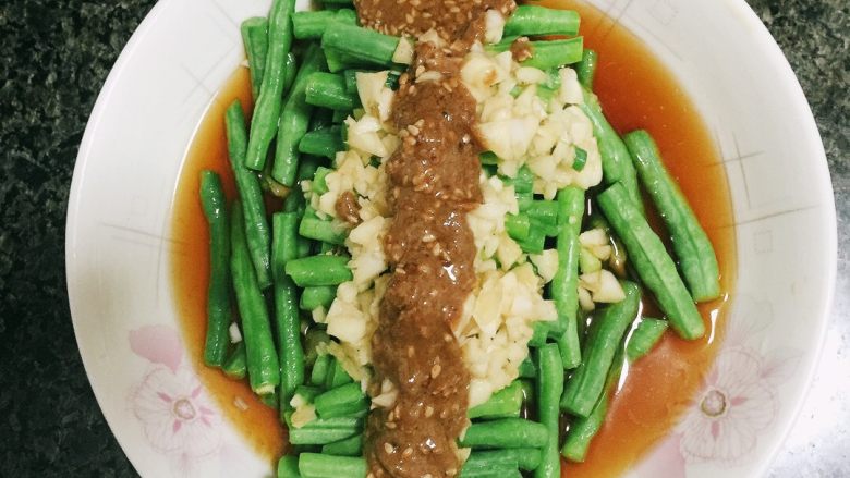 凉调豆角,最后,摆盘,然后用生抽,醋,盐和鸡精调汁,把切碎的蒜倒入汁中,一起浇在摆好的豆角上,最后爱吃芝麻酱的可以在上面在铺上适量的芝麻将,好吃的要咬掉自己的舌头