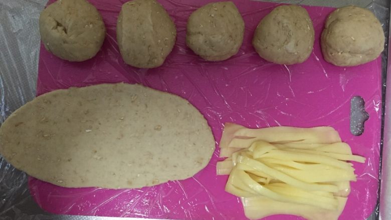 燕麦芝士贝果~,把小面团揉成椭圆形,再用擀面杖擀成椭圆形大面皮~将芝士切成条,容易包裹~