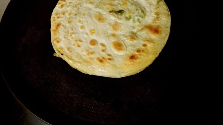 葱油鸡蛋饼,饼铛加热,涂少许油,放入擀好的饼,烙至一面上色,将其翻面。