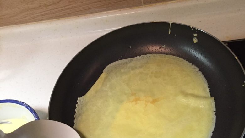 榴莲千层,舀一勺饼皮液,迅速让液体在锅内以流动的方式散开成饼皮状,用平滑的勺子从边上翻起饼皮,不要翻破了。