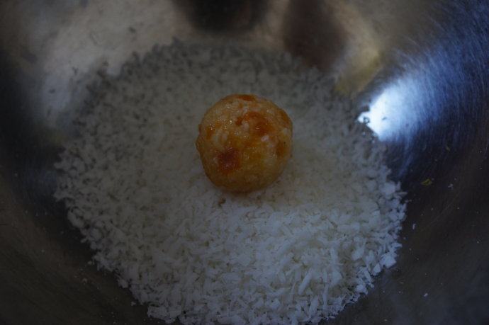 椰香黄杏球和姜味生巧克力,把小球放入剩余的3/4杯椰丝里,均匀裹上椰丝。