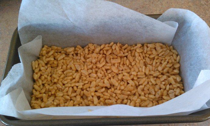 儿时记忆——花生巧克力糖米花,将一半泡泡米压入铺好烘培纸的模具里(用涂油的勺子压紧)